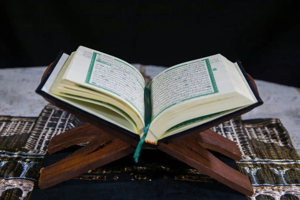 An open Quran placed on a wooden stand with visible Arabic calligraphy, symbolizing faith and tradition.